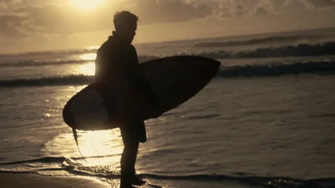 Backlit surfer walking to the ocean and doing the cross religious sign Stock Footage 307316671