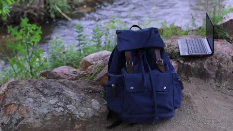 Backpack and laptop of a digital nomad in the jungle next to a river Stock Footage 130186133