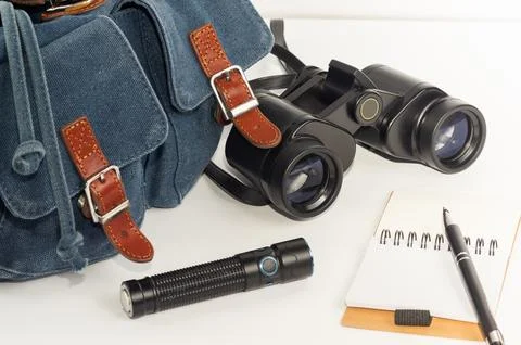 Backpack, binoculars, flashlight, and notebook in close-up against a white .. Stock Photos