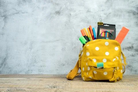 Backpack with different colorful stationery on table. Grey concrete backgroun Stock Photos