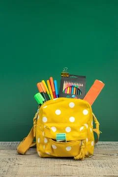 Backpack with different colorful stationery on table. Green background. Bac.. Stock Photos