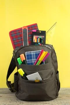 Backpack with different colorful stationery on table. Yellow background. Ba.. Stock Photos