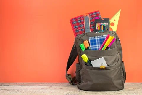 Backpack with different colorful stationery on table. Orange background. Back Stock Photos