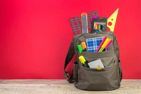 Backpack with different colorful stationery on table. Bright Red background.  Stock Photos