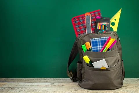 Backpack with different colorful stationery on table. Green background. Back  Stock Photos