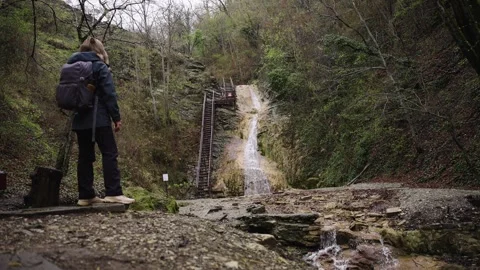 Backpack Equipped Hiker Walking Along Mossy Path Towards Forest Waterfall Stock Footage 310232546