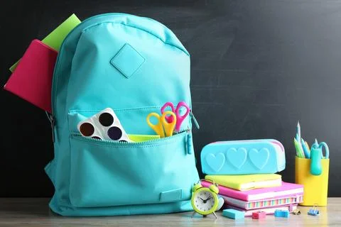 Backpack full of different school stationery on table near chalkboard Stock Photos