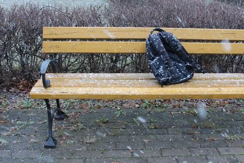 Backpack left on a snowy bench in a quiet park during winter Stock Photos