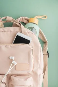 Backpack with notebook, phone, bottle, and earphones on green background Stock-Fotos