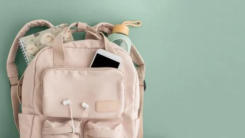 Backpack with notebook, phone, bottle, and earphones on green background Stock Photos