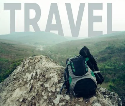 Backpack on peak of cliff in front of word travel. Stock Photos