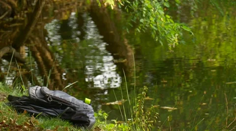 Backpack is Placed on Lake Bank Fresh Green Trees Rippling Water Forest in Warm Stock Footage 68597997