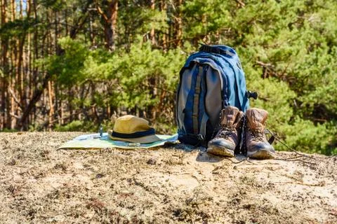 Backpack, touristic boots, map, compass and hat on a ground in a coniferous f Stock Photos