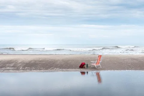 Backpack, yerba mate container and thermos next to a beach chair reflected in Stock Photos