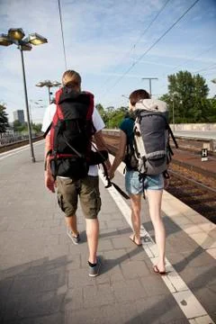 A backpacker couple walking on down a train platform Stock Photos