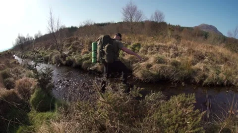 A backpacker crossing a mountain stream 動画素材 207997721