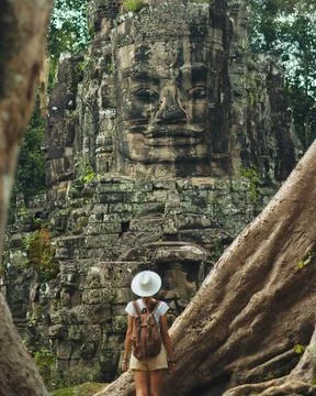 Backpacker Facing Bayon Face Tower Through Roots, Angkor Thom Cambodia Foto stock