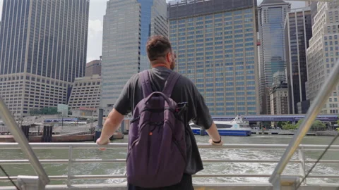 Backpacker at ferry rail facing Financial District towers New York City New. Vidéo 348193918