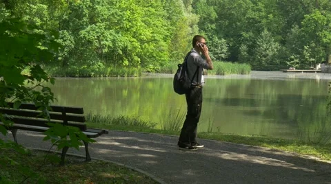 Backpacker Makes a Call on Mobile Phone Standing in Alley Walking by Park Stock Footage 63811281