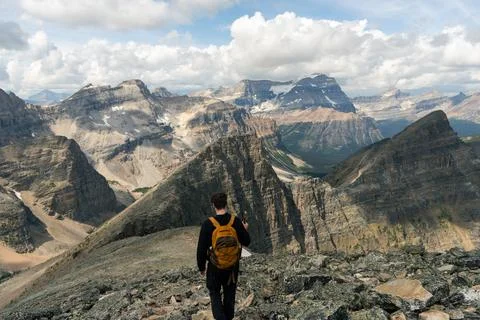 Backpacker overlooking a vast mountain range under cloudy sky. Stock Photos