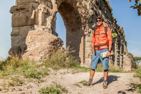Backpacker posing under majestic ancient roman aqueduct at sunset. Young Stock Photos