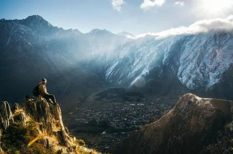 Backpacker sit on cliff edge and looks at mount valley Stock Photos