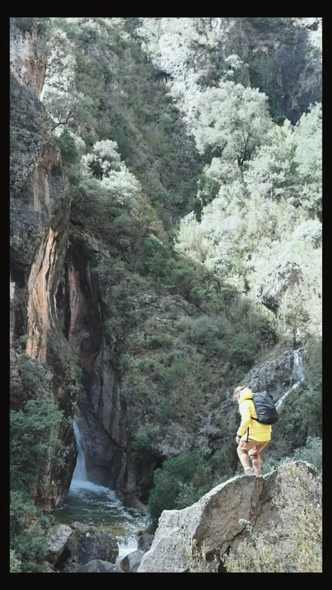 Backpacker standing on rock outcrop with open arms near waterfall Stock Footage 304030587