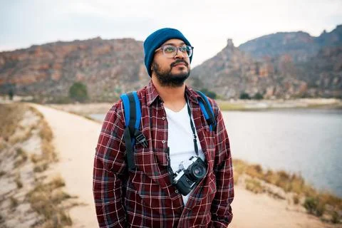 A backpacker stares out into the mountains while hiking with camera next to lake Stock Photos