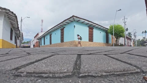 A backpacker turning the corner of vibrant blue house with wooden shutters. 動画素材 338033587