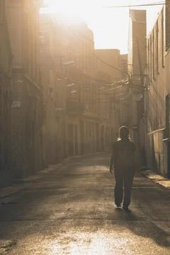 Backpacker walking alone down urban street at sunset Stock Photos