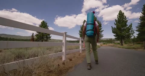 Backpacker Walking Along Countryside Road with Mountains Stock Footage 323354688