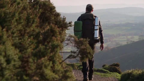 A backpacker walking around a corner overlooking lush green English countryside 動画素材 260242735