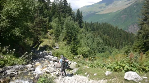 Backpacker walking over a creek with mountain in background Stock Footage 43248829