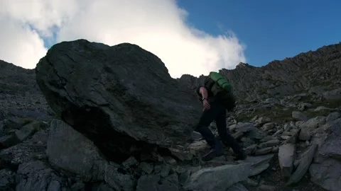 A backpacker walking past a huge rock in the mountains 動画素材 164234497