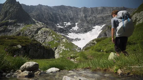 Backpackers hiking along river in meadows with mountain panorama, 4K Stock Footage 129611711