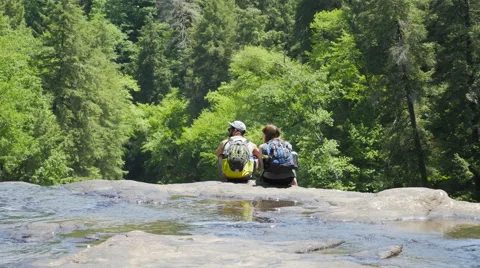 Backpacking Couple Sitting on Waterfall Ledge Overlooking Forest Stock Footage 50564227