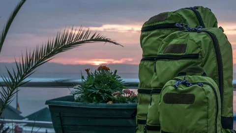 Backpacks of different sizes stand near the sea at sunrise behind the clouds Stock Footage 76297524