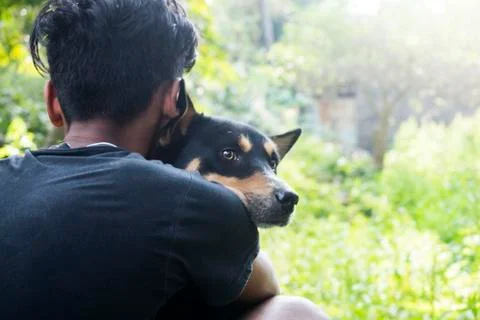 Backside of a boy hugging his pet dog in front of natural background. the dog Stock Photos
