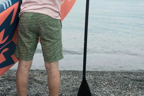 Backside section of young man with paddle board and paddle about to enter sea Stock Photos