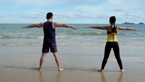 Backside video of Young couples doing exercise in the beach in the morning Stock Footage 132664713