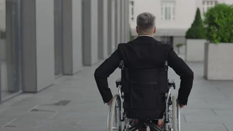 Backside view of man in suit moving while sitting in wheel chair at street. Male Stock Footage 146510765