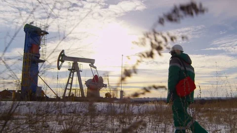 Backside View Worker Walks along Oil Field with Well and Derrick Video stock 79477073