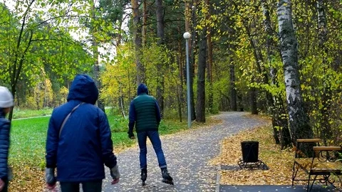 Backside view young people skate rollers along park track Stock Footage 98892995