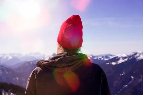 Backside of young man looking into the distance surrounded by mountain peaks Stock Photos