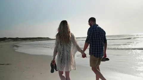 Backview of couple holding hands walking on beach Video stock 83359559
