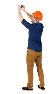 Backview of an engineer in construction helmet stands and using Backview o... 库存照片