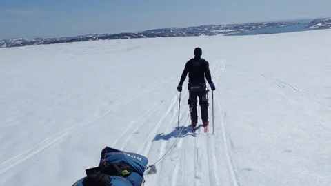 Backview of explorer skiing though Greenland glacier and coast in the background 스톡 동영상 129512764