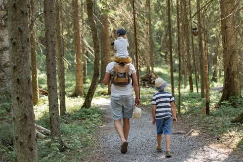 Backview of man walking alone the leane in forest with two sons. One boy is 写真素材
