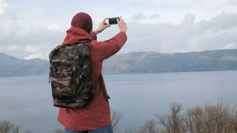 Backview of one trendy guy in color jacket take a pic of beautiful natural scene Stock Footage 199493082