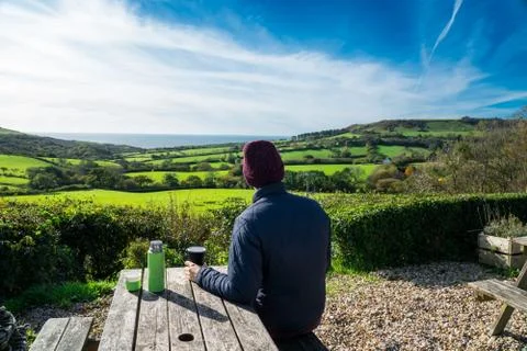 Backview young man in warm clothes sitting in farmer wooden cafe and enjoying Stock Photos